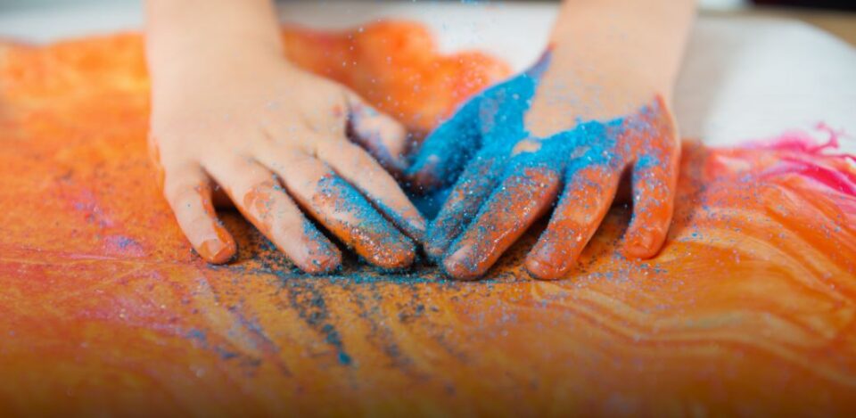 a child hands with blue and orange paint on them. Coral Autism program EA schools Ohio