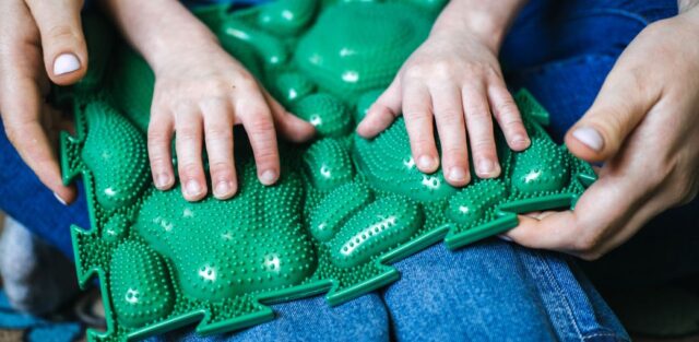 a child's hands on a green sensory massage mat for autism - Education alternatives