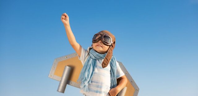A child wearing an aviator hat and goggles. And cardboard wings, channelling their energy and learning impulse control through imaginative play.