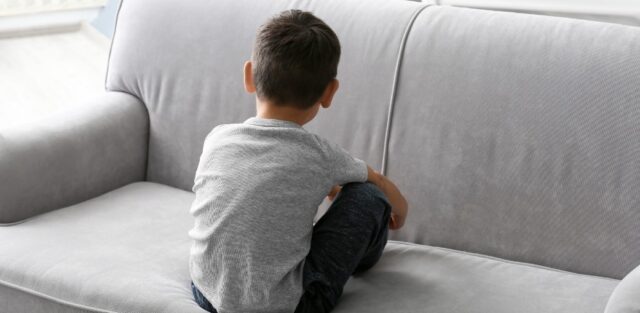 Young child sitting on a sofa with their back turned, representing the early signs of autism and raising the question of who can diagnose autism.