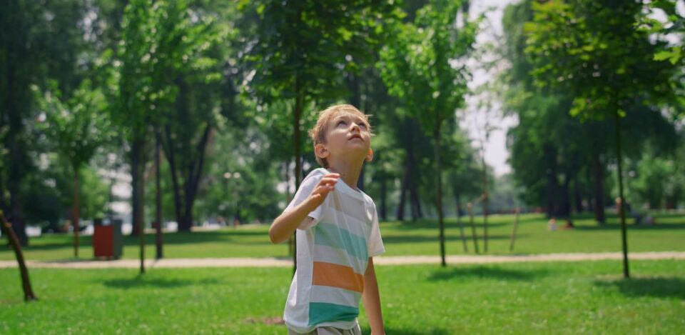 Young boy in a striped shirt looking up in a park, illustrating signs of autism in 4 year old children such as sensory awareness or focused attention. Education Alternatives, Ohio.