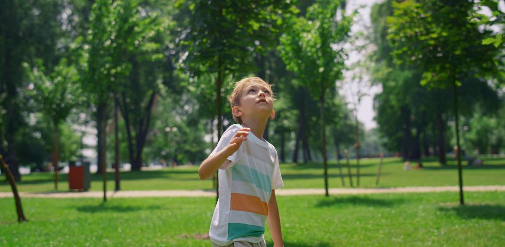 Young boy in a striped shirt looking up in a park, illustrating signs of autism in 4 year old children such as sensory awareness or focused attention. Education Alternatives, Ohio.