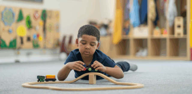 A young child playing with a wooden train set on the floor, illustrating a calm developmental moment often discussed in guides about what are the different levels of autism. EA schools, Ohio.