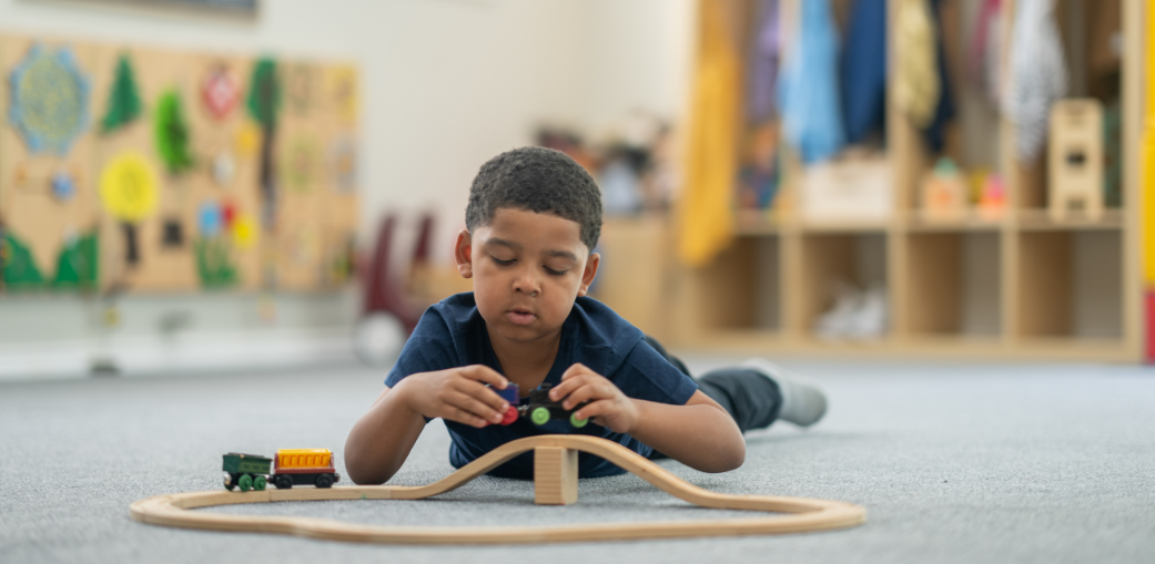 A young child playing with a wooden train set on the floor, illustrating a calm developmental moment often discussed in guides about what are the different levels of autism. EA schools, Ohio.