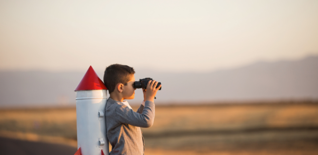 A child looking through binoculars next to a toy rocket. EA Schools Ohio