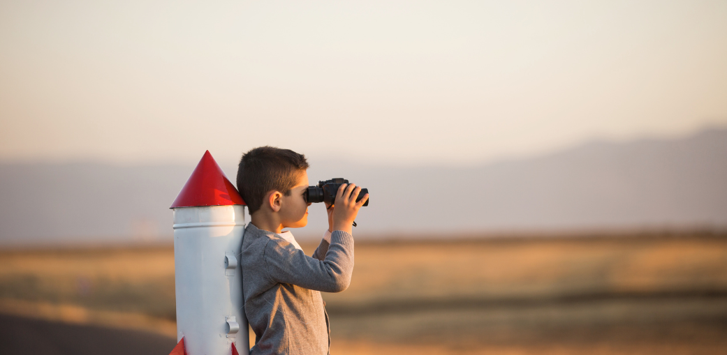 A child looking through binoculars next to a toy rocket. EA Schools Ohio