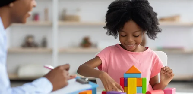 A child playing with colorful building blocks while being observed by a specialist, providing a helpful visual for parents researching the differences between autism-related behaviors and laughing seizures.