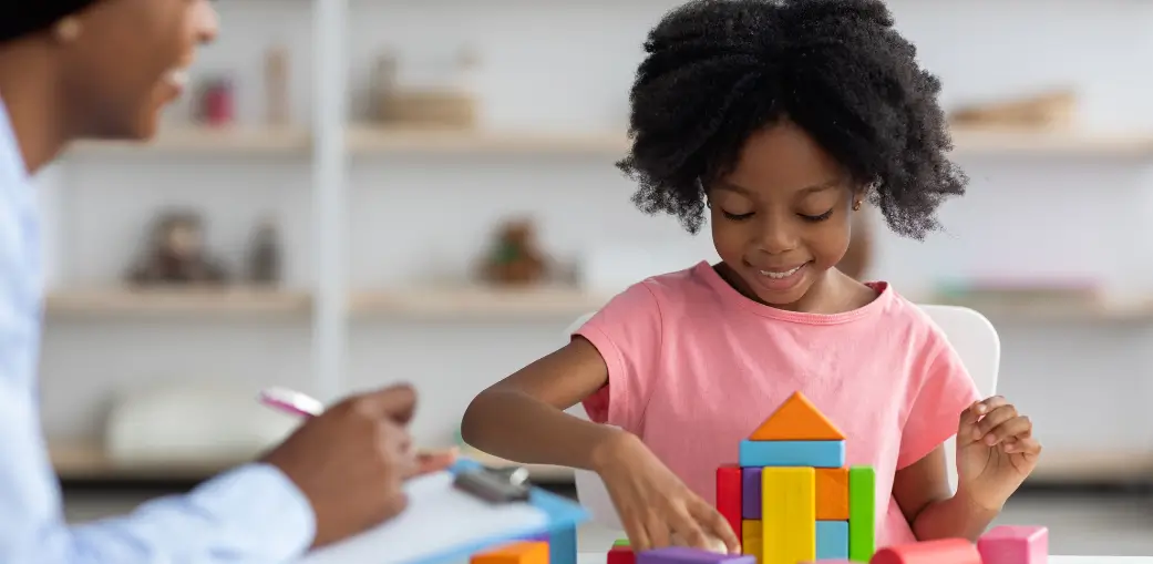 A child playing with colorful building blocks while being observed by a specialist, providing a helpful visual for parents researching the differences between autism-related behaviors and laughing seizures.