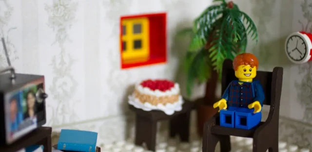 LEGO child figure sitting alone in a chair watching television in a small room, symbolizing how autism behaviors can feel isolating or misunderstood to others. Autism behavior. EA School. Ohio