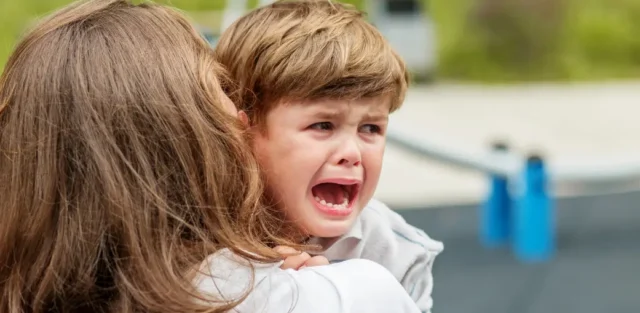Alt text: Parent holding and comforting a young child who is crying and distressed, illustrating autism yelling and screaming during an overwhelming moment. Education Alternatives School. Ohio