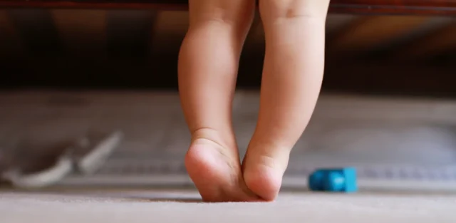 Toddler walking on tiptoes on a carpet at home, a possible early sign of autism