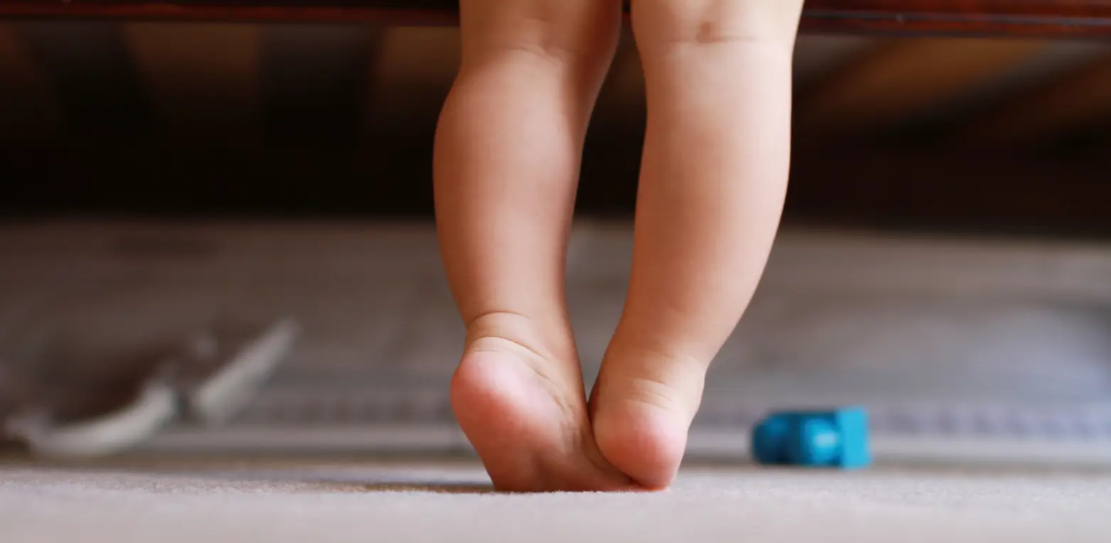 Toddler walking on tiptoes on a carpet at home, a possible early sign of autism